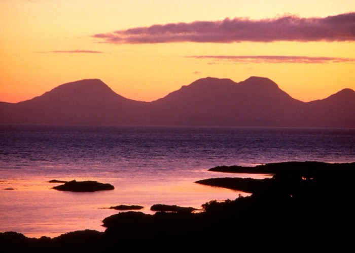 Uitzicht op de kenmerkende silhouetten van de Paps of Jura (de drie hoogste toppen van het eiland: Beinn an Òir, Beinn Shiantaidh en Beinn a’ Chaolais) op het eiland Jura, bij zonsondergang, Binnen-Hebriden.
